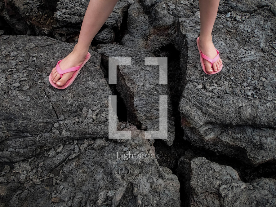 feet in flip flops standing over a crack in volcanic rock