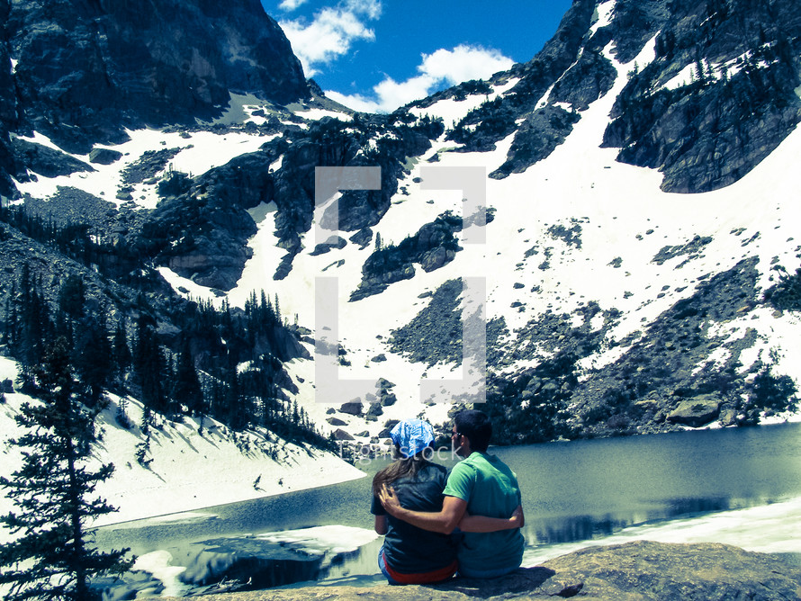 couple sitting in front of a mountain lake 