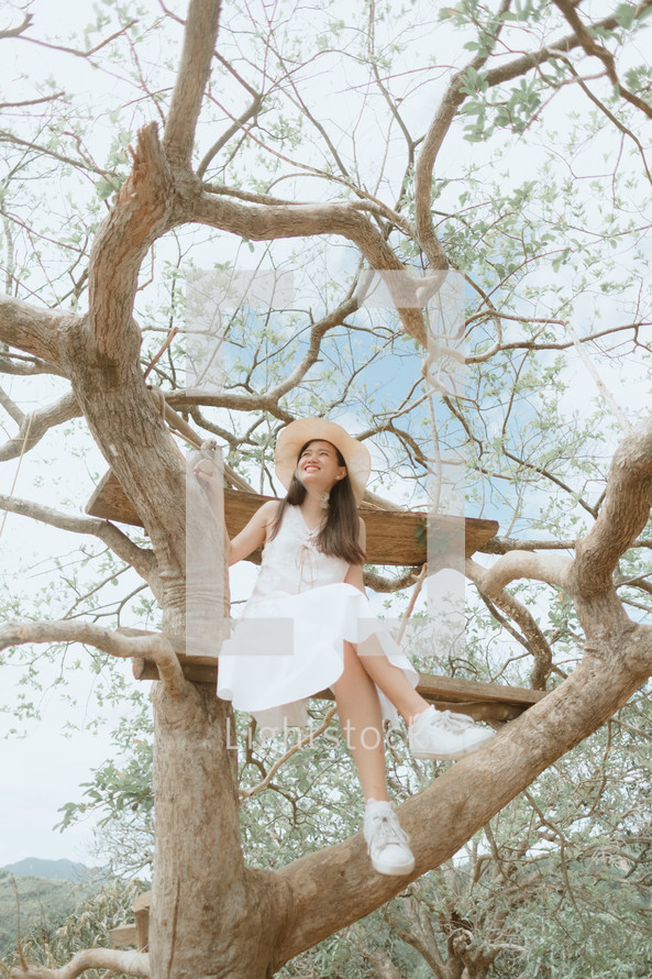 woman with a straw hat sitting in a tree 