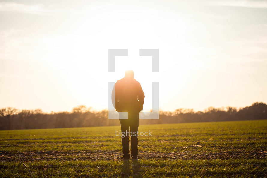 silhouette of a man in a field with his hands in his pockets and his head down