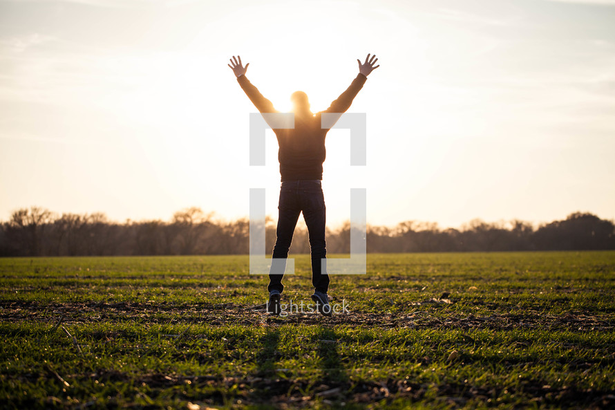 man jumping in a field with his hands raised