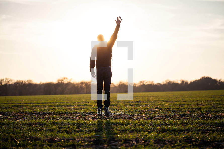silhouette of a man jumping in a field with his hand raised to God