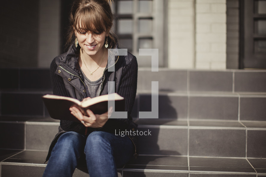 woman sitting on stairs reading a Bible