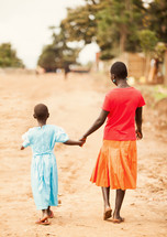 woman and girl walking holding hands on a dirt road