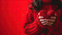 Female hands in red knitted sweater holding heart shape on red background