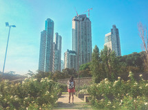 A woman walking on a garden path on the outskirts of a big city.