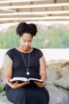 an African American woman sitting outdoors reading a Bible 