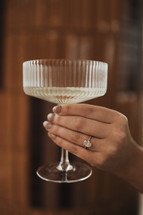Hand holding a champagne glass with engagement ring
