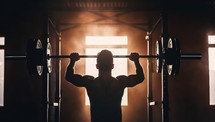 Back view of a man lifting a barbell in a gym.