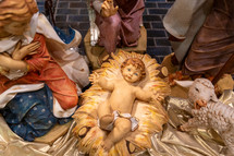 View from above of baby Jesus lying on the manger. He is surrounded by Mary, Joseph, an angel, and a lamb