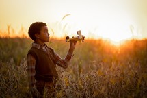 a child with a toy airplane in a field at sunset 