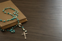 Rosary with blue beads on a book on a black background