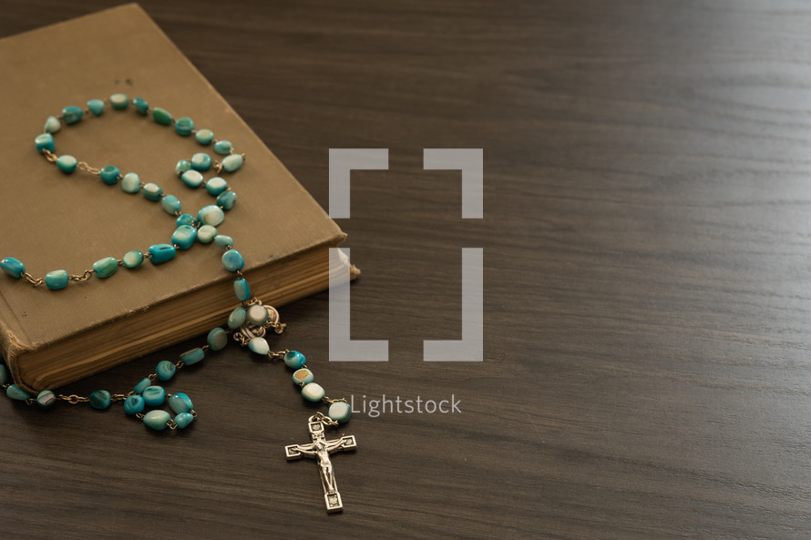 Rosary with blue beads on a book on a black background