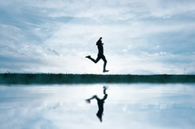 man jumping in the field and reflecting in the lake
