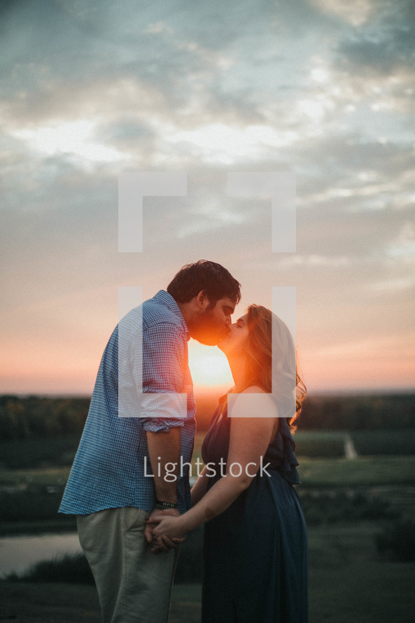 a couple kissing outdoors at sunset 