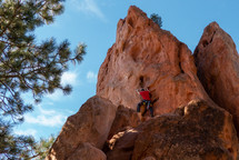 rock climber on side of rugged rock with pleasant lighting, evergreen, and blue sky