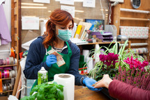 Young caucasian woman at work in a nursery. The florist wears a mask and gloves to avoid the infection of the coronavirus covid-19. The photo shows a customer paying with euro coins and banknotes.