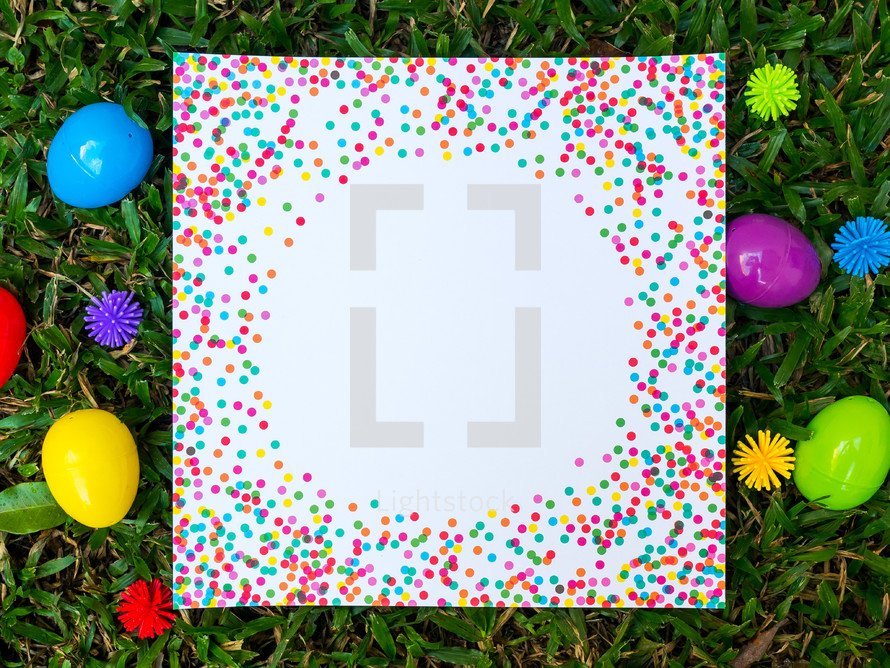 A colorful piece of paper and Easter eggs in green grass.