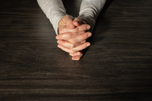 Hands folded in prayer on a dark wood table with copy space