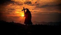 Silhouette of a man holding a cross at sunset background.