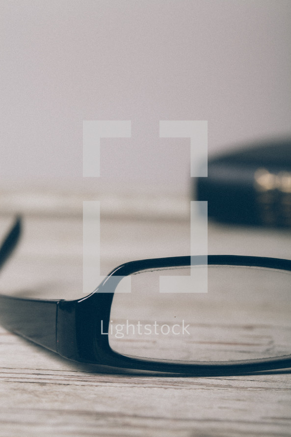 single lens of a pair of reading glasses and a Bible