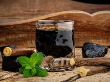 Licorice liqueur with pure blocks, root and fresh mint on wooden table.