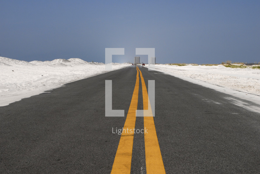 Open road through white sand dunes with double yellow lines