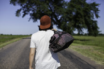 man standing in the middle of a road with his back to the camera carrying a bag
