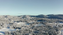 Aerial shot flying through a snowy landscape filled with snow covered trees and forests as well as farms