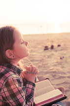 young girl praying on the beach with her bible; sunset