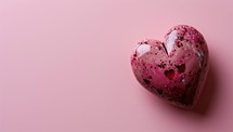 A speckled heart shaped object on a pink background