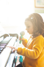 Girl toddler plays the piano and sings with the toy microphone