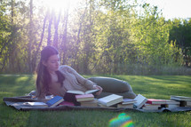 a teen girl reading books on a picnic blanket 