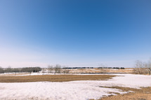 Blue sky and agricultural field with snow melting in spring