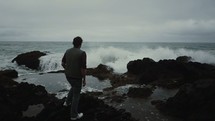 a man watching the waves crash into a rocky shore 