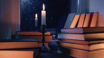 Stack of old paper books on wooden windowsill, bathed in soft candle glow light. Cozy ambience of fall, candle burning. Literature promotions or tranquil visual storytelling. Rainy autumn weather.