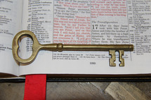 Brass skeleton key on the pages of a Bible opened to Matthew 16:19, laid on a wooden table. keys kingdom saint peter catholic