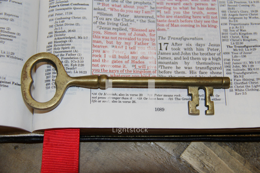 Brass skeleton key on the pages of a Bible opened to Matthew 16:19, laid on a wooden table. keys kingdom saint peter catholic
