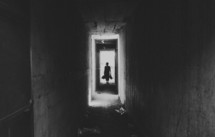 Person standing in a doorway at the end of an old hallway