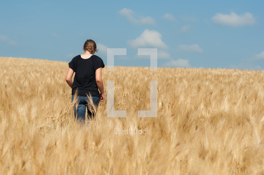 woman walking through a field of wheat 