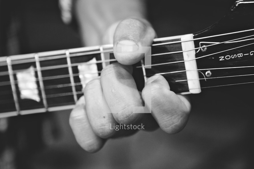 Man's hand holding neck of guitar.