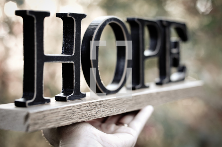 Hand holding a board with letters spelling "hope."