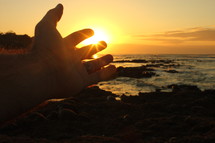 reaching hand at sunrise and the ocean 