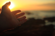 reaching hand at sunrise and the ocean 