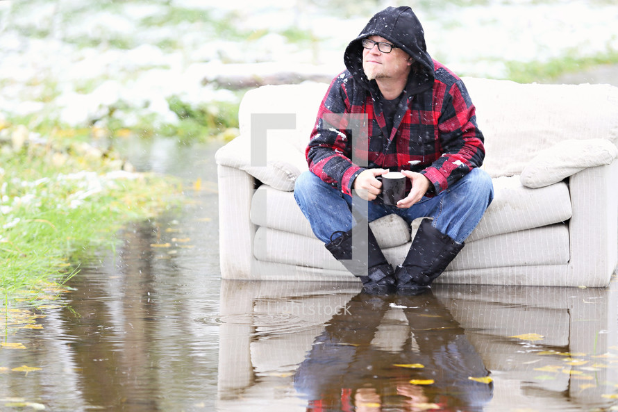 A man sits on a couch that is outside in water.