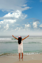 girl standing on a beach with raised hands 