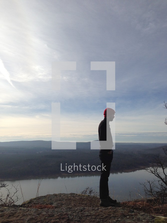 man standing at the edge of mountain top looking out over a lake