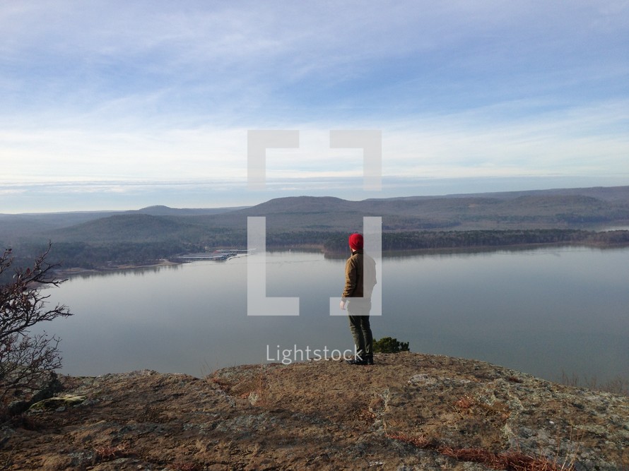 man standing at the edge of a mountain top looking out over a lake