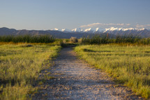 dirt road leading to snow capped mountain peaks 