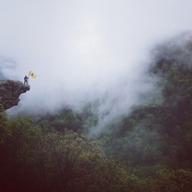 man holding a yellow flag a the edge of a steep drop off in the mountains